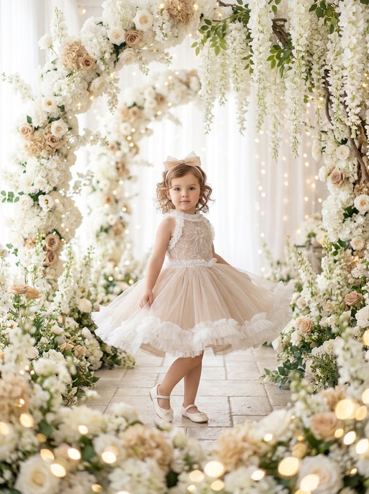 Front view of a child wearing a beige dress with a white floral-patterned bodice and white ruffled hem.