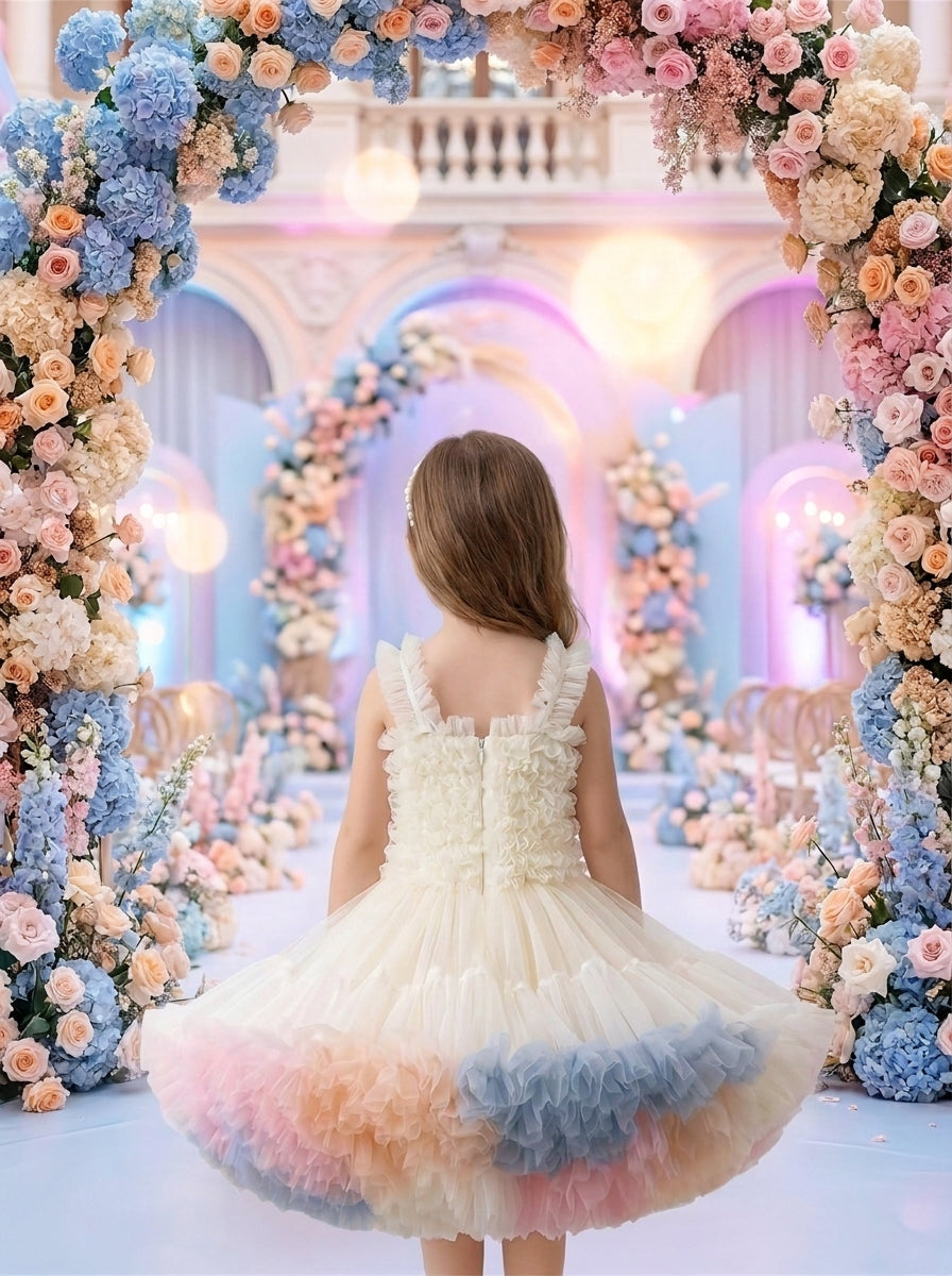 Back view of a child wearing a cream ruffled dress with pastel pink, peach and blue skirt panels.